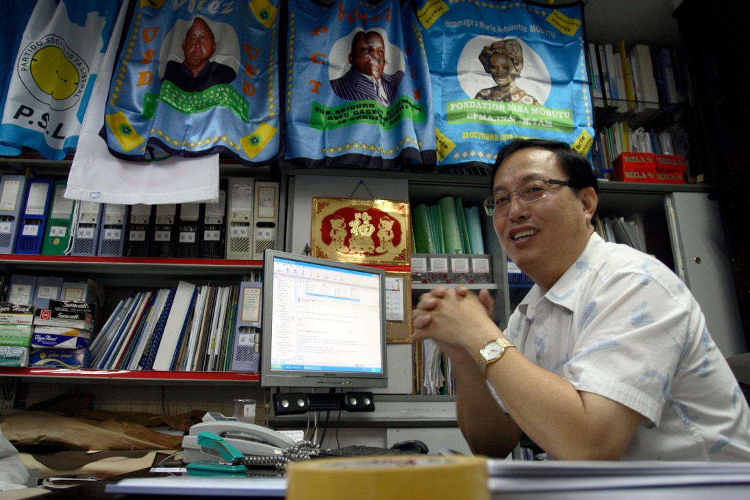 Patrick Yung, owner of National Sonic, sits at his desk with African political posters displayed on the wall behind him.