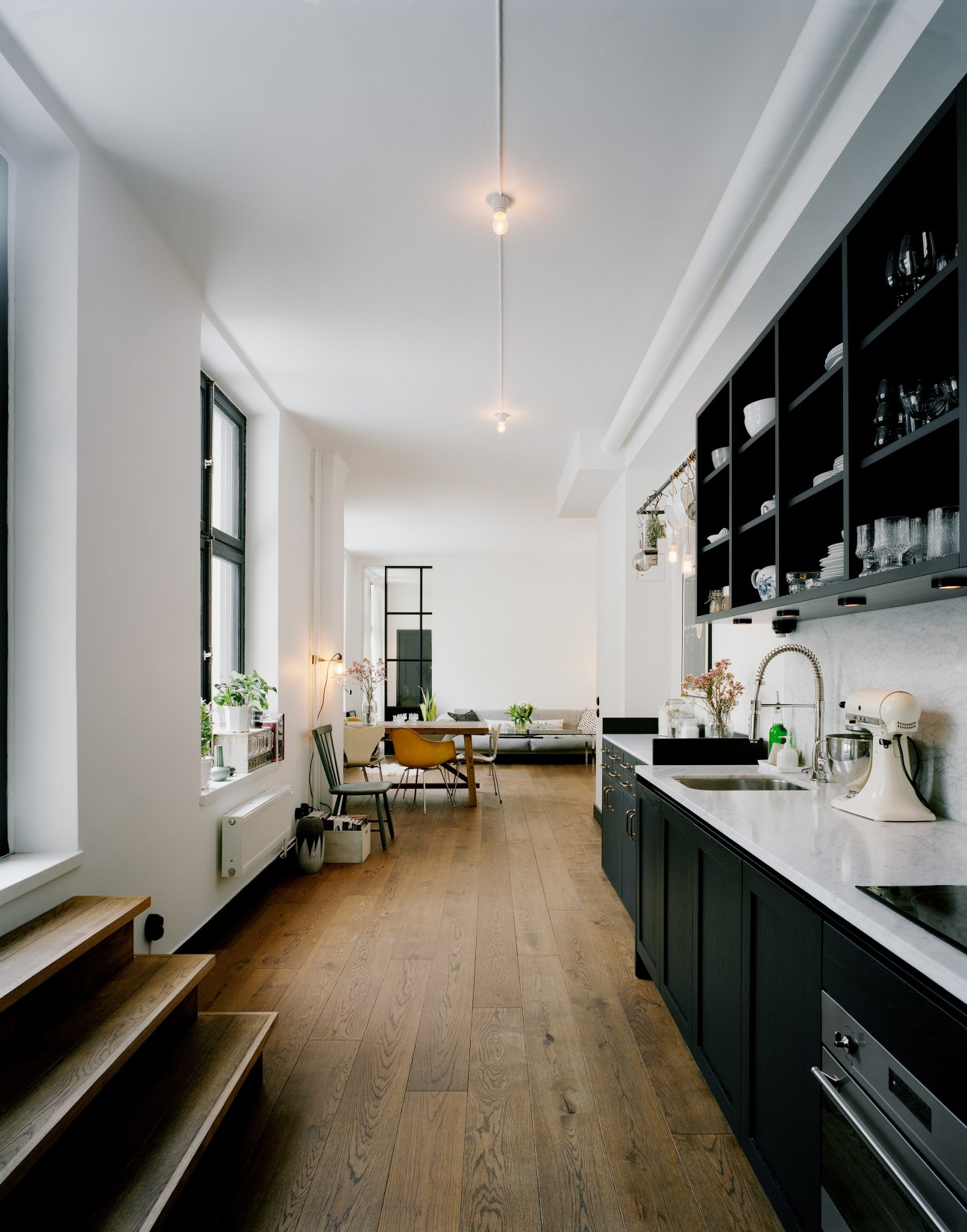 Open-plan kitchen and living room with dark cabinetry, marble countertops, oak flooring and pendant lights.