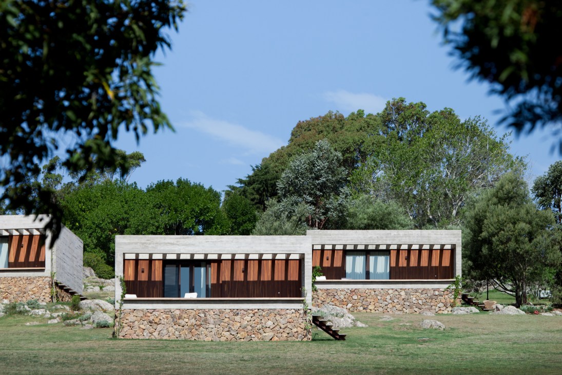 Modern single-storey bungalows with stone foundations and wood cladding nestled among trees at Las Piedras Fasano.