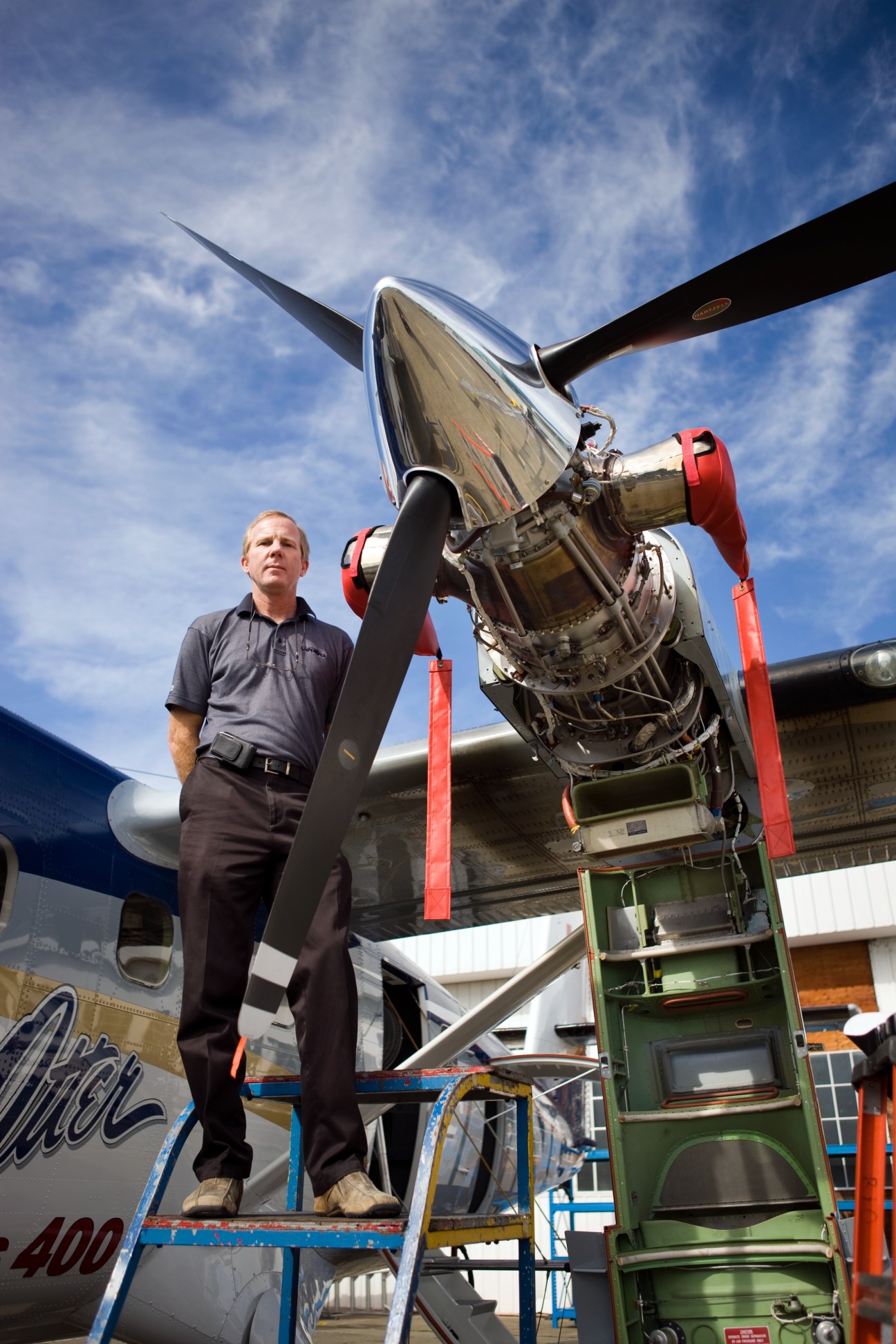 Steve Stackhouse, Viking Air's manager of flight operations, stands on a ladder next to a de Havilland aircraft engine.