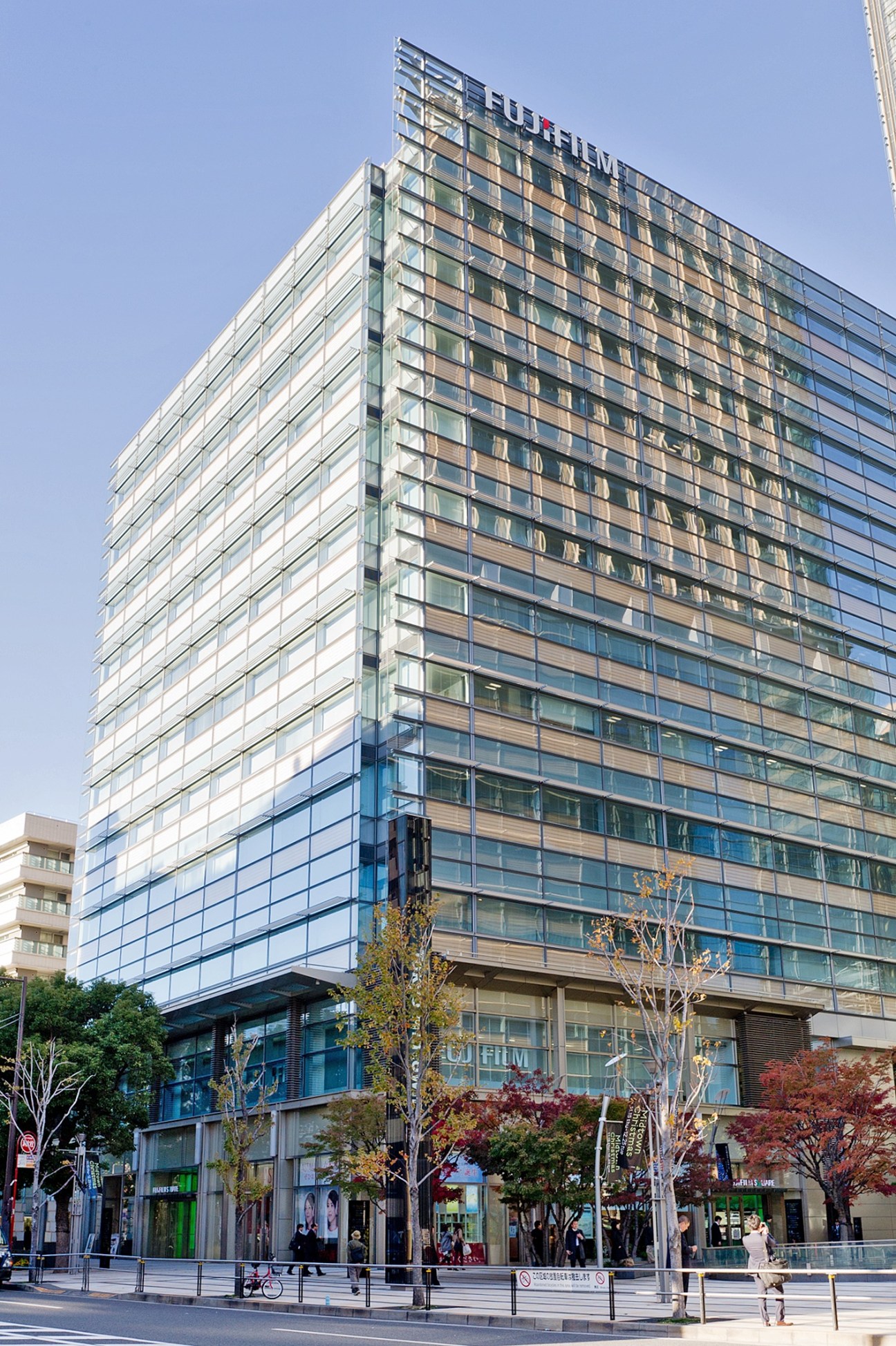 Fujifilm's modern glass and metal headquarters building at Tokyo Midtown with street-level retail spaces.