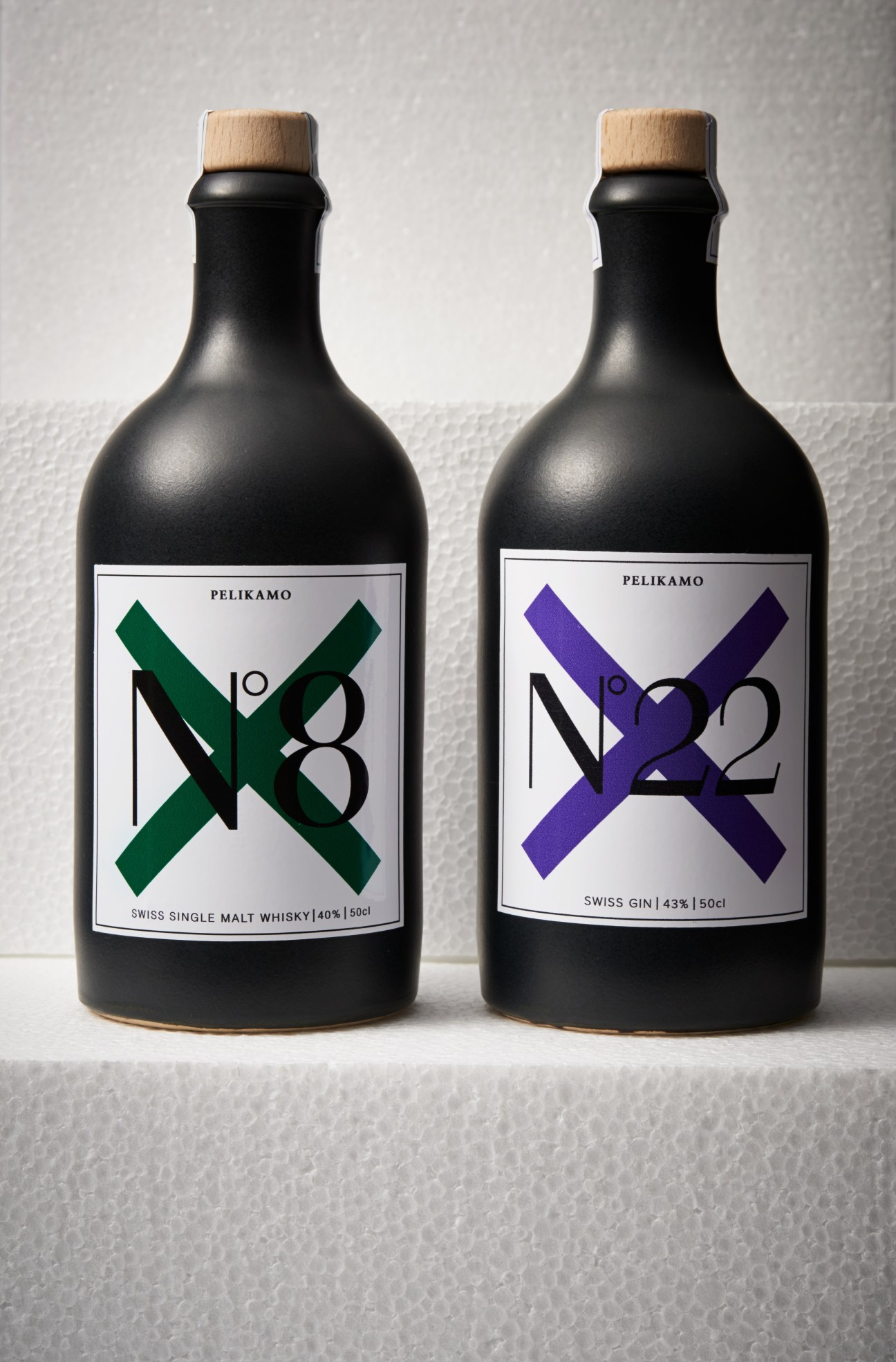 Two black bottles of Pelikamo spirits with wooden cork tops and geometric labels in green and purple.