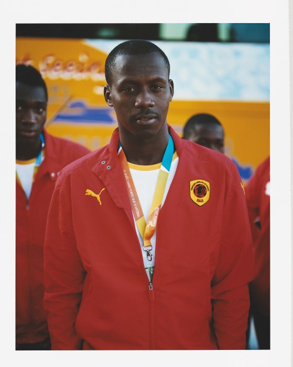Man in red Angolan team tracksuit with Puma logo and national crest, wearing medal on lanyard.