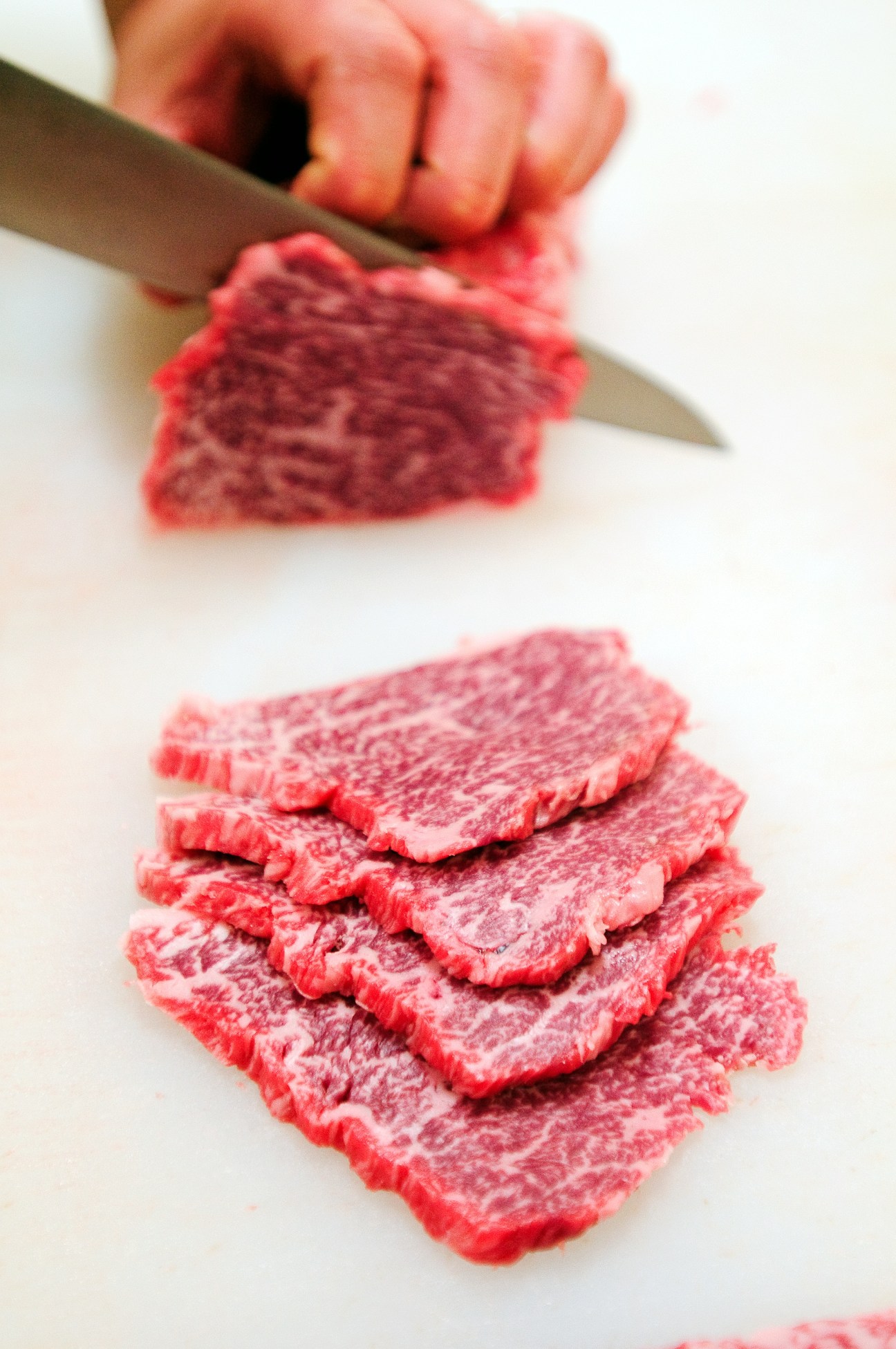A butcher's hands slicing wafer-thin strips of marbled Omi beef with a knife.