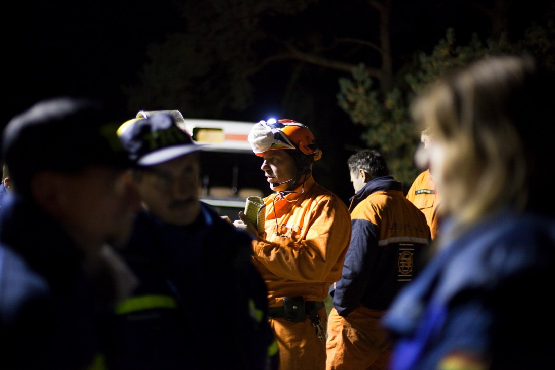 Dutch rescue worker in orange uniform and headlamp leads team briefing at night training event.