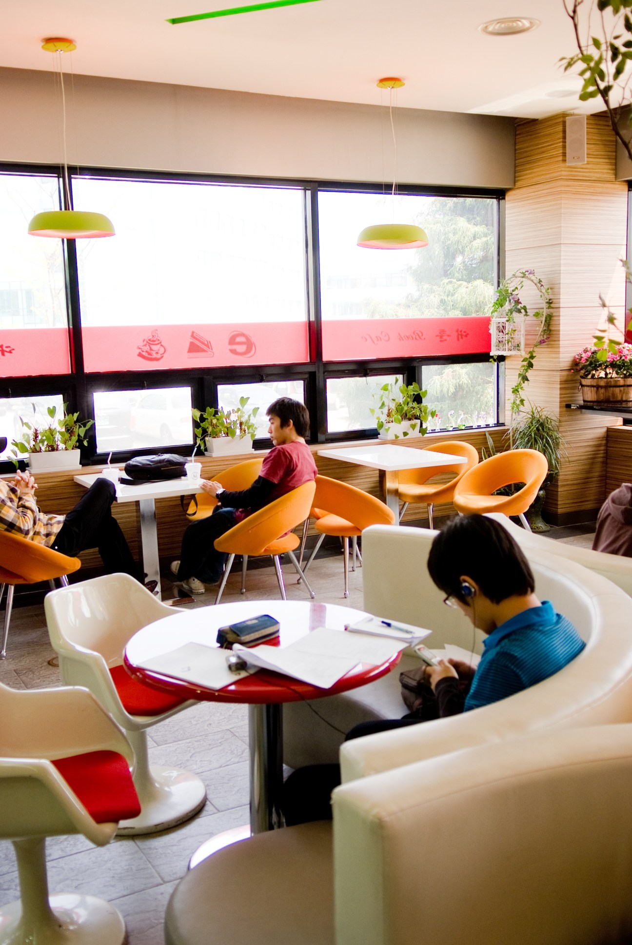 Students studying in KAIST's Book Café with modern furniture and large windows overlooking campus grounds.