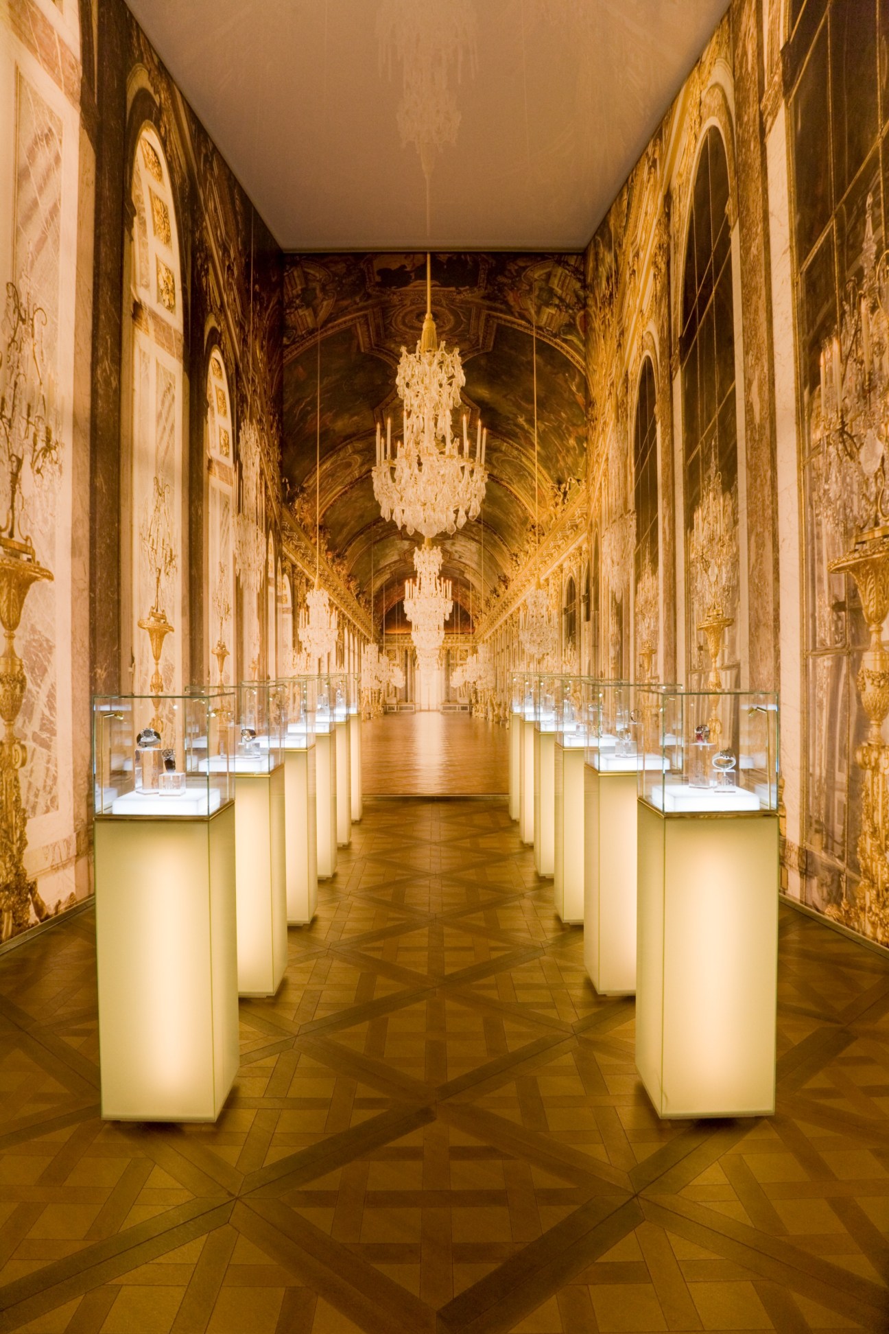 Ornate baroque-style corridor with gold decorative walls, crystal chandelier, and illuminated display cases showcasing watches.