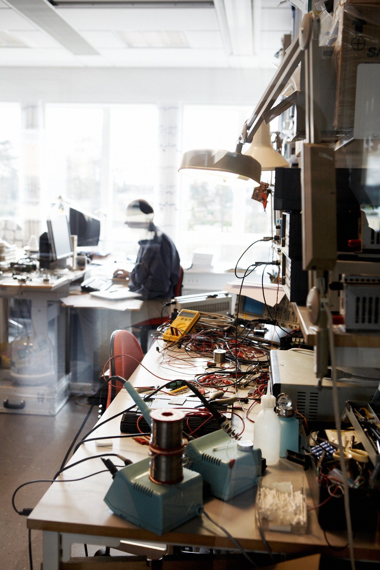 Electronics testing workbench with various equipment, cables, and instruments in a bright office laboratory.