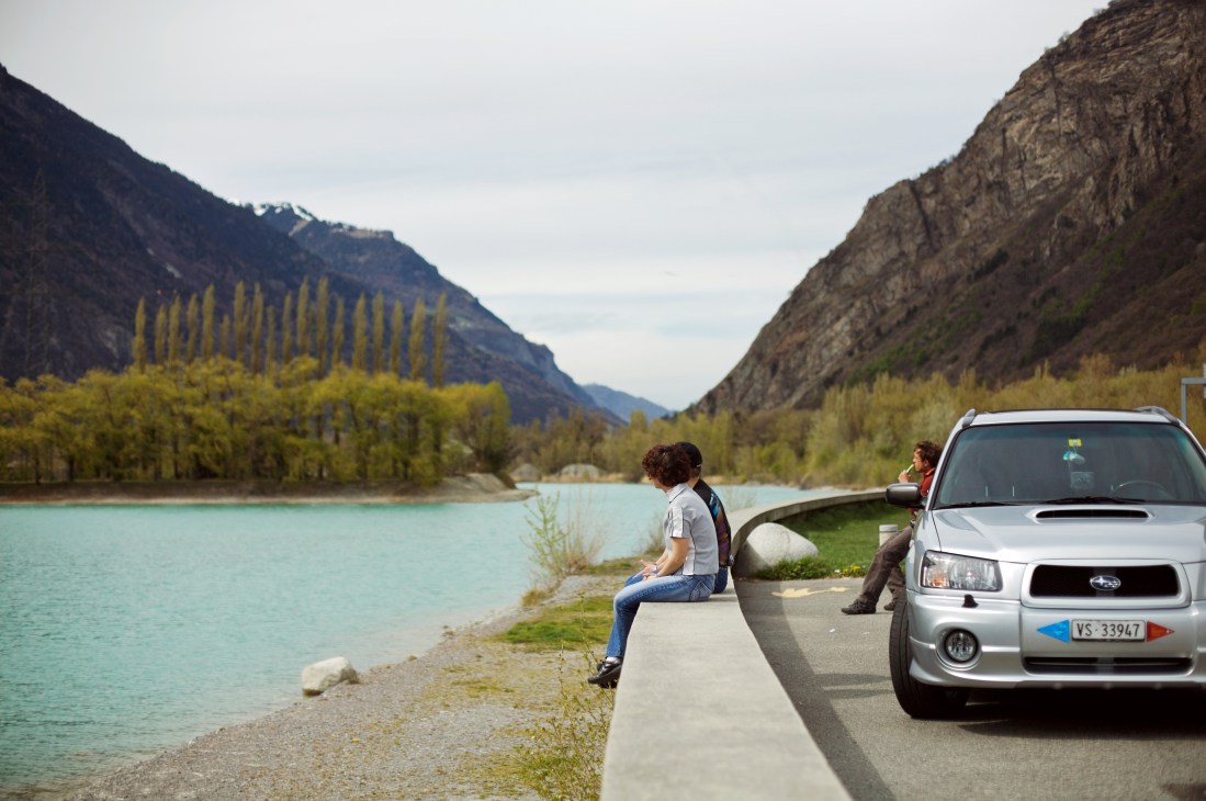 Anne-Joëlle and Jean-Raphaël Fumeaux with their silver Subaru Forester Turbo parked by a turquoise alpine lake.
