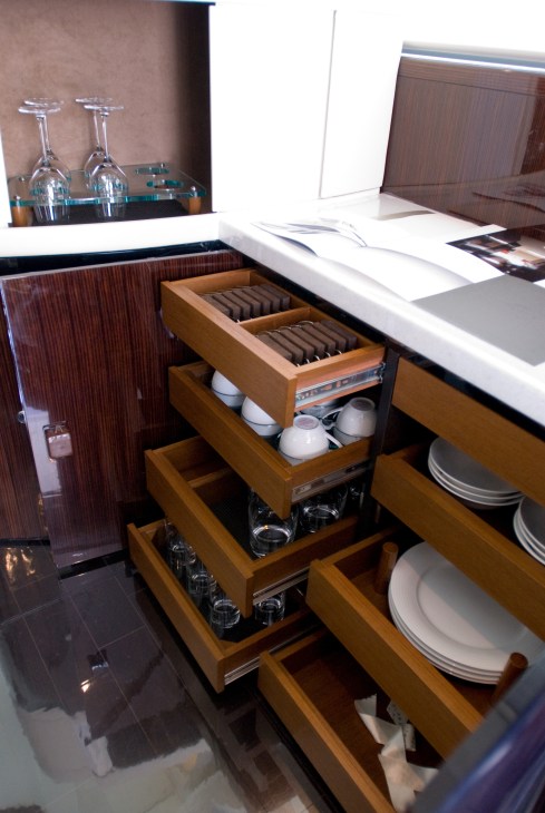Interior of boat showing organized wooden drawers with tableware, glasses, and accessories.