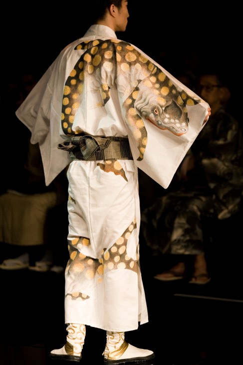 Male model wearing a white cotton-silk yukata with crocodile pattern and gold circular motifs, styled with a dark obi belt.