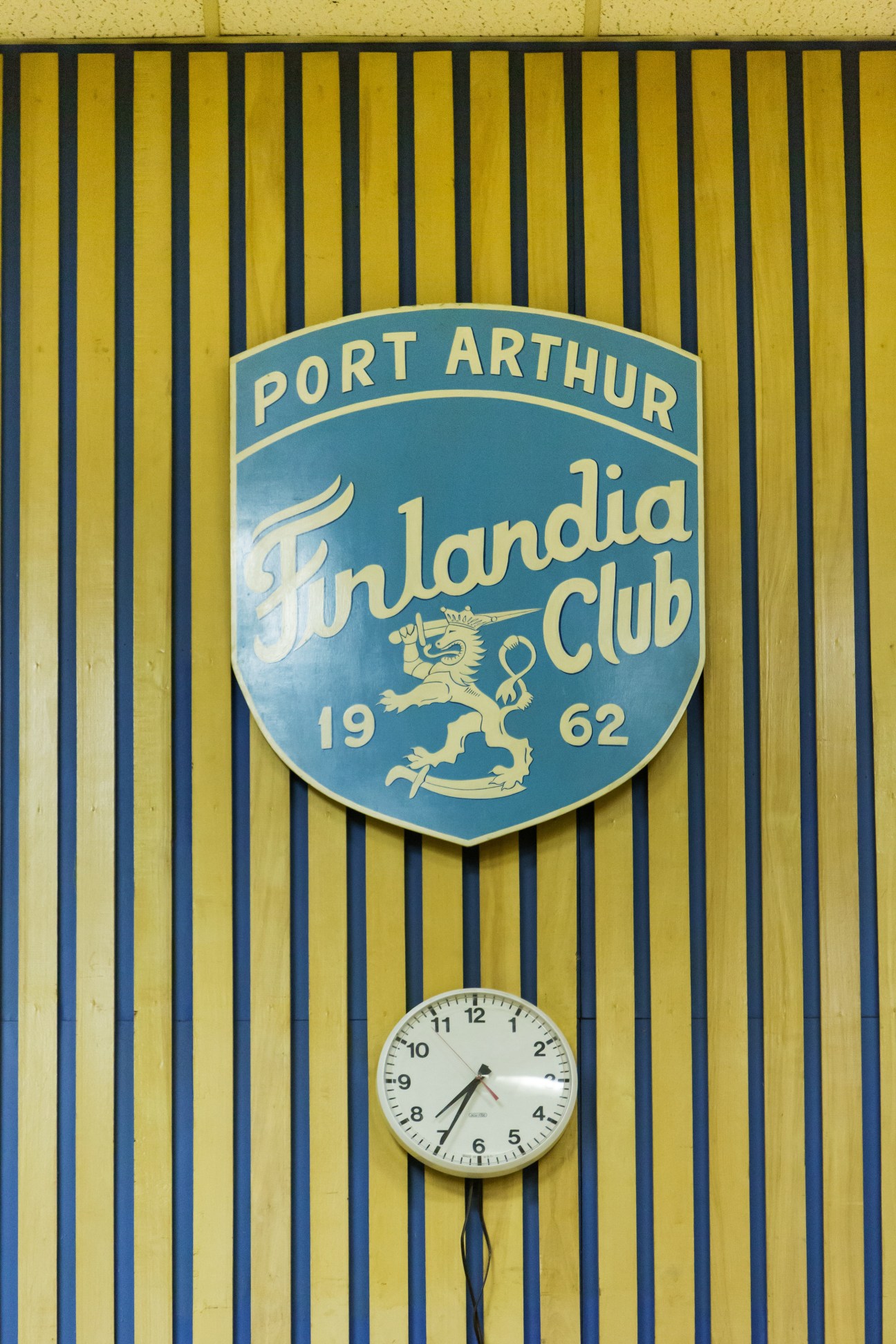 Port Arthur Finlandia Club shield dated 1962 mounted on yellow corrugated siding with clock below