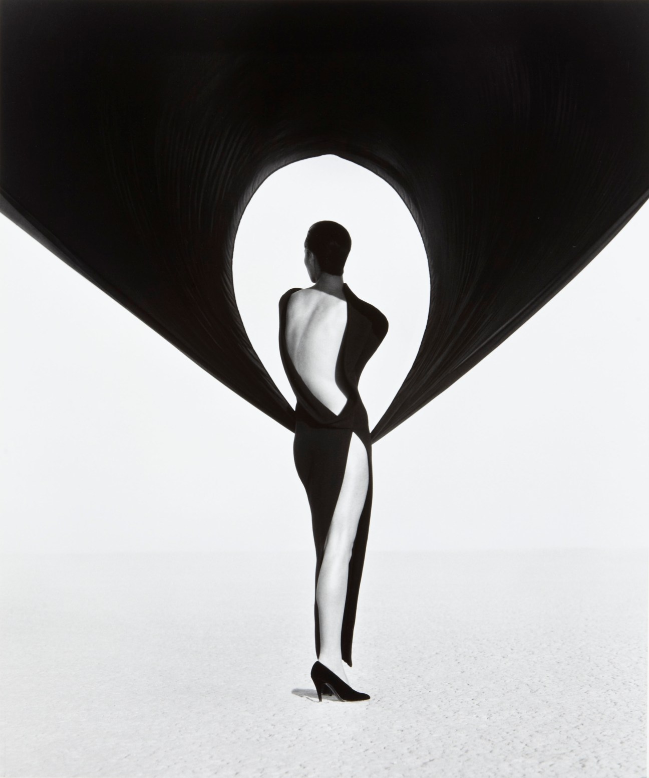 Black and white photograph of a model in a Versace dress photographed from behind against a light background.