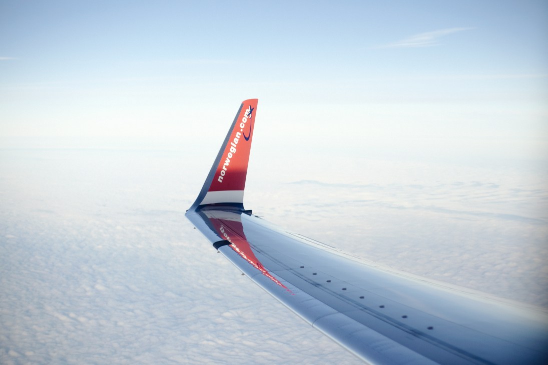 Norwegian airline aircraft wing and tail fin against cloudy sky