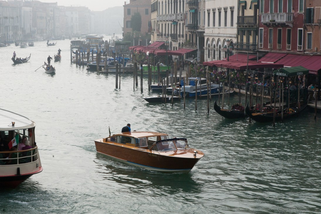 Water taxi navigating the Grand Canal in Venice with historic buildings and gondolas along the waterfront.