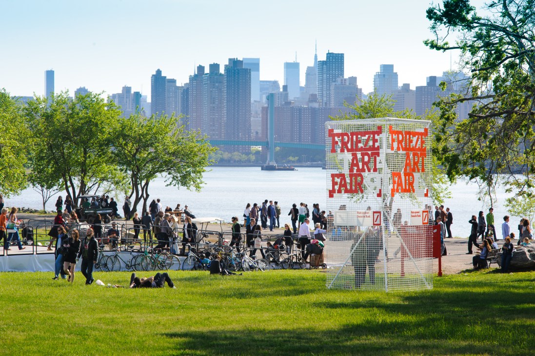 Frieze Art Fair booth with red signage on a waterfront lawn overlooking Manhattan skyline.