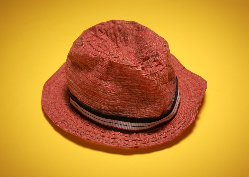 Red hemp-fibre sun hat by Grevi with striped fabric band against yellow background.