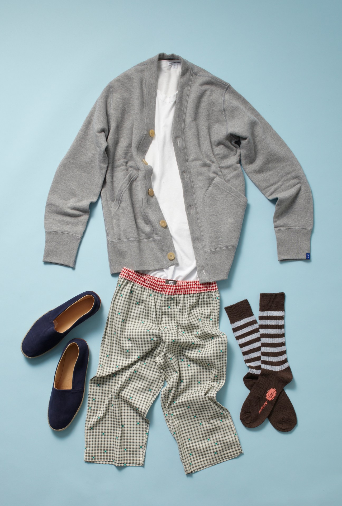 Grey cardigan, white t-shirt, checkered trousers, striped socks and navy suede espadrilles arranged flat on light blue background.