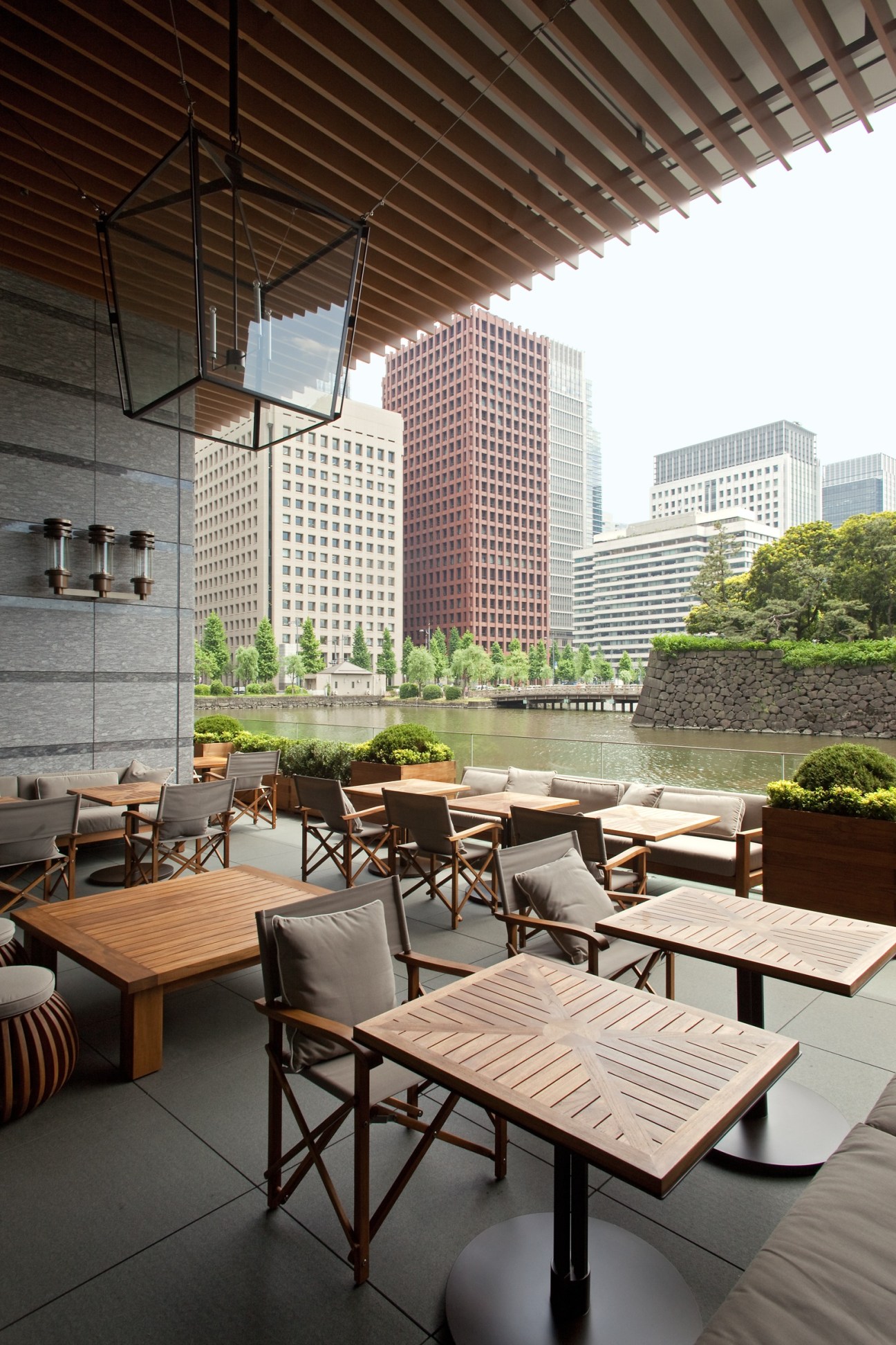 Modern hotel terrace with wooden furniture overlooking a river and city skyline.