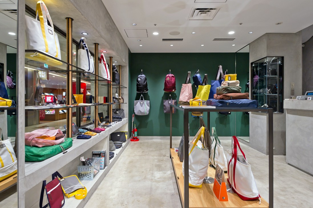 Interior of Bijirushi shop at Narita airport displaying colorful backpacks and travel bags on green walls and wooden tables.