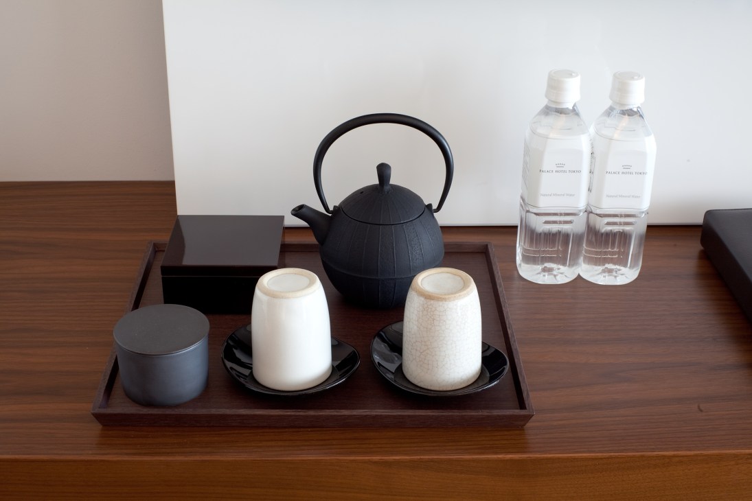 Palace Hotel Tokyo room amenities including black teapot, ceramic cups, water bottles, and toiletries on wooden tray.