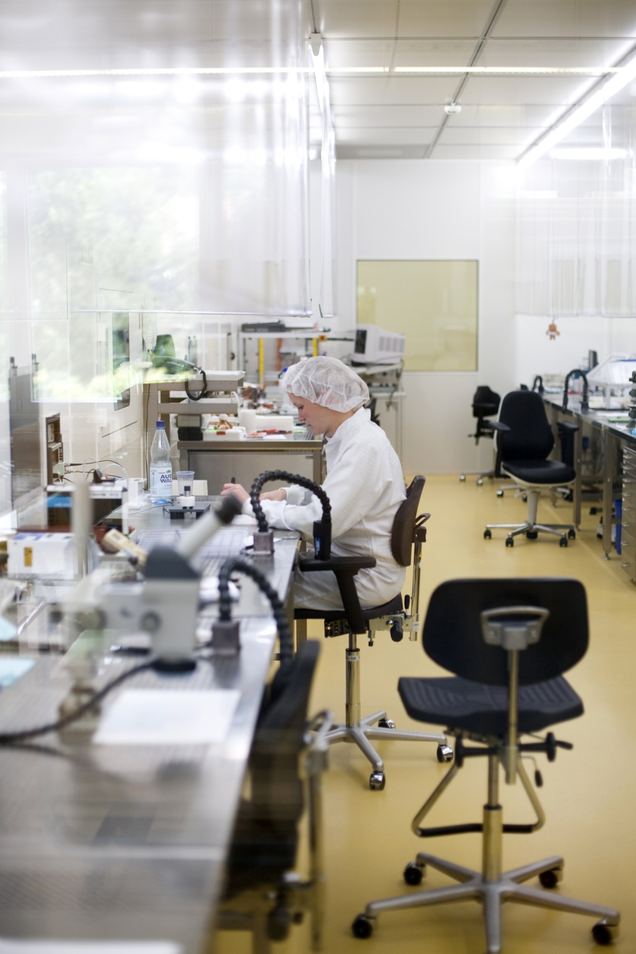 Woman in white coat and hair net working at workstation in a clean room laboratory.