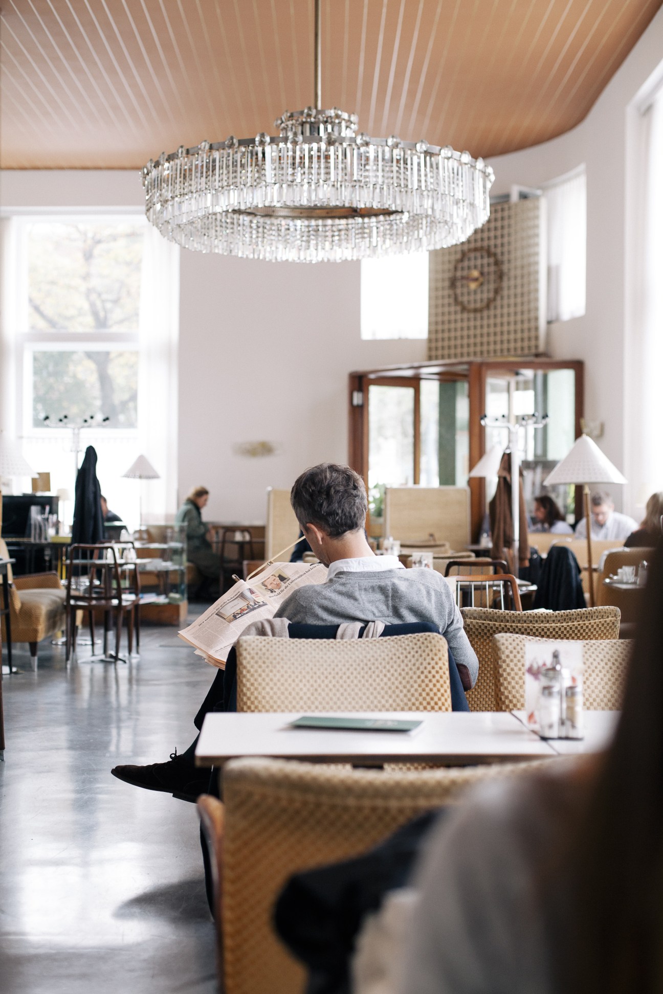 Man reading newspaper in modernist café with crystal chandelier and mid-century furnishings