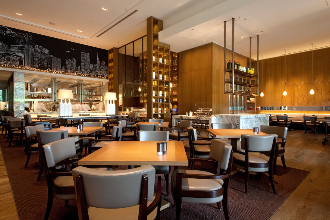Modern hotel restaurant interior with wooden paneling, dining tables, and illuminated shelving at Palace Hotel Tokyo.