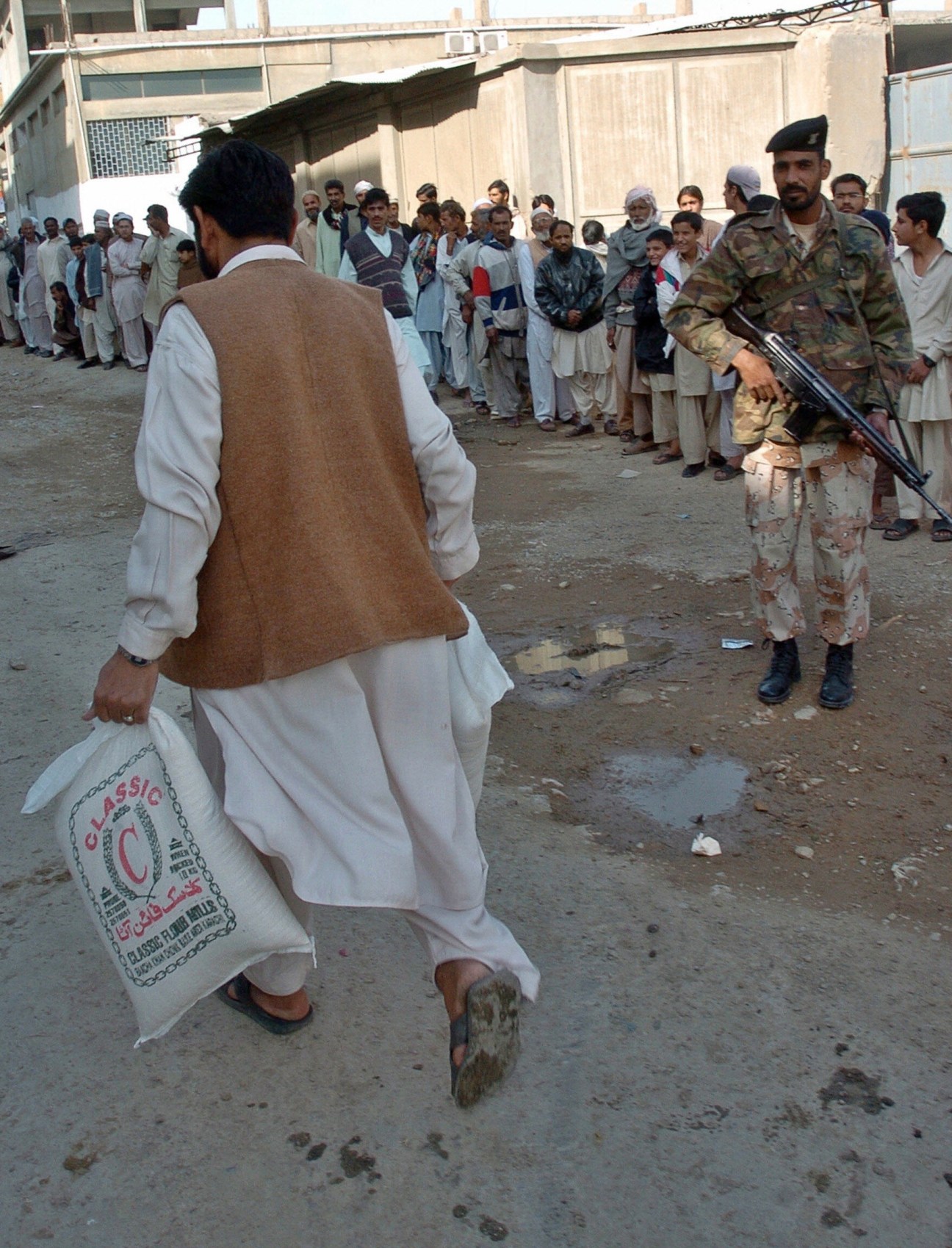 A soldier stands guard as people queue outside a flour mill in Karachi to buy government-subsidised flour.