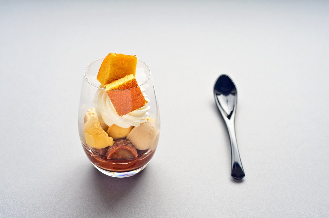 ANA's layered parfait dessert with orange peel garnish and whipped cream in a glass with spoon.