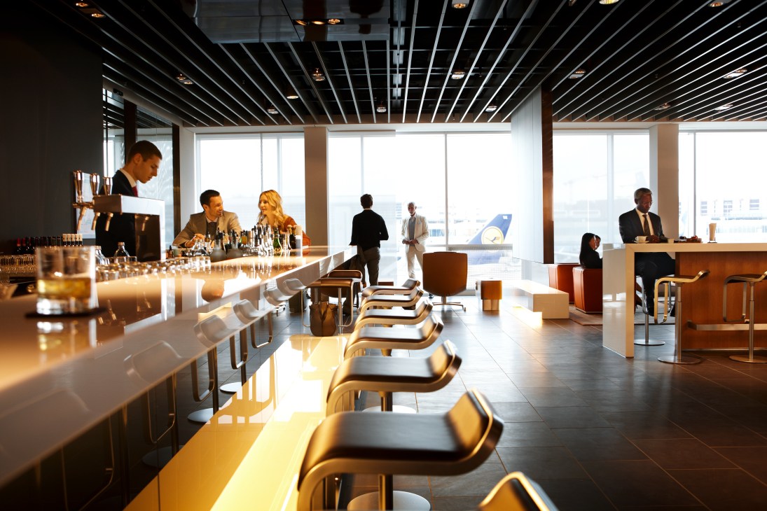Modern airport lounge with long counter seating, floor-to-ceiling windows, and business travelers.