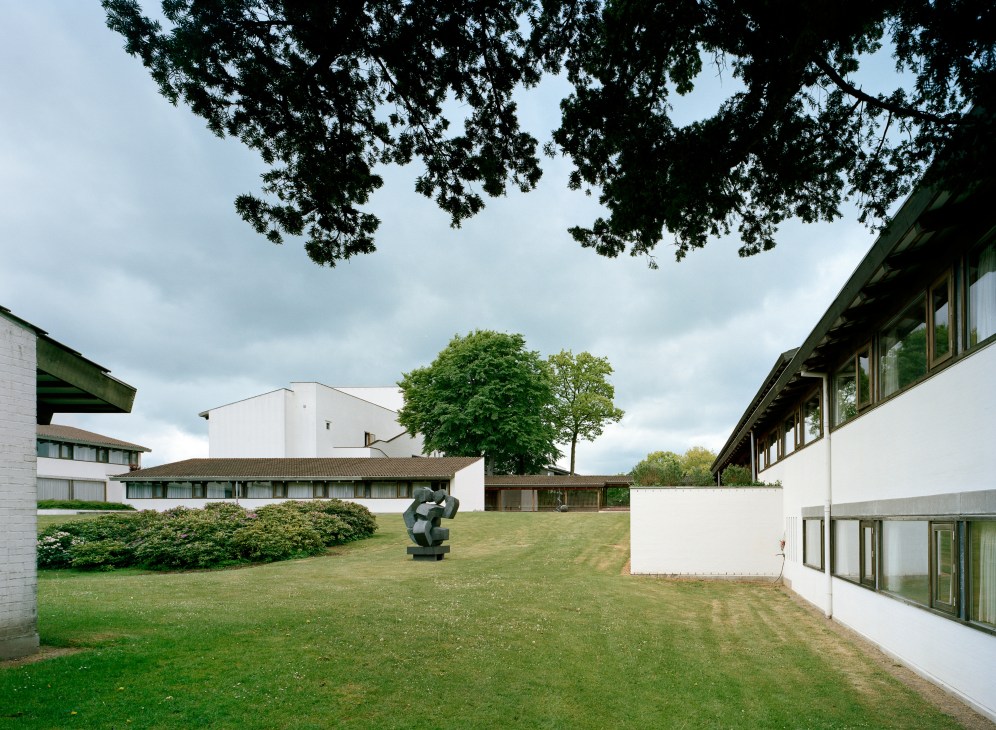 Lo-skolen's white brick buildings and sculpture scattered across green parkland with mature trees.