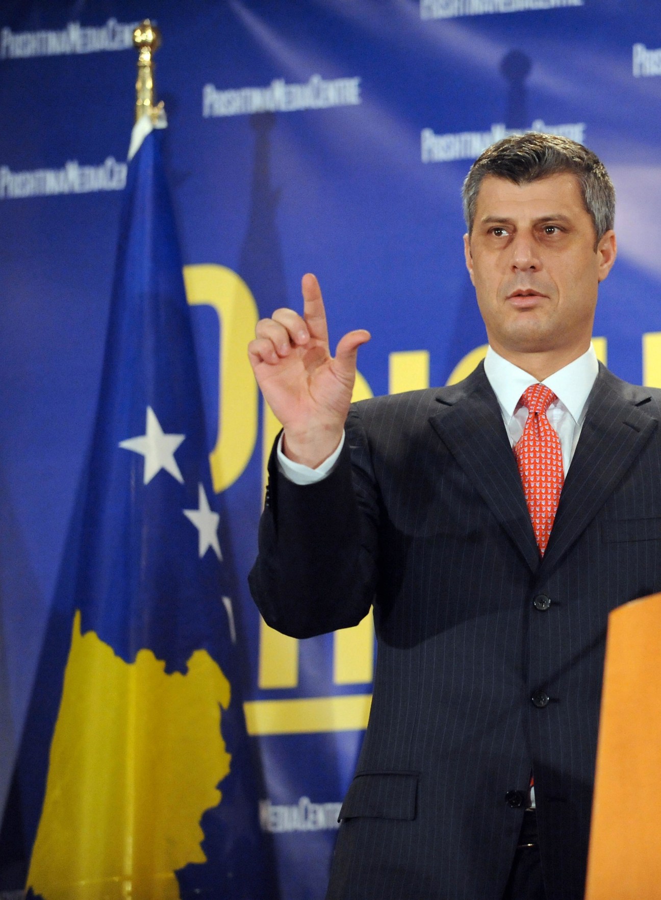 Prime Minister Hashim Thaçi at a press conference with Kosovo's blue and yellow flag behind him.