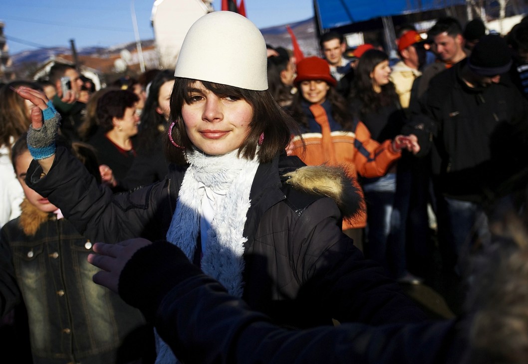 A Kosovo Albanian woman wearing a traditional white hat and blue and white scarf celebrates in Mitrovica.