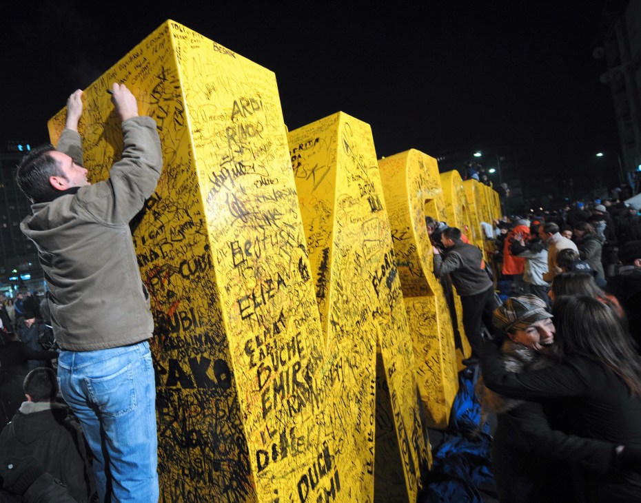 A man signs a large yellow monument displaying 'New Born' during Kosovo independence celebrations in Pristina.
