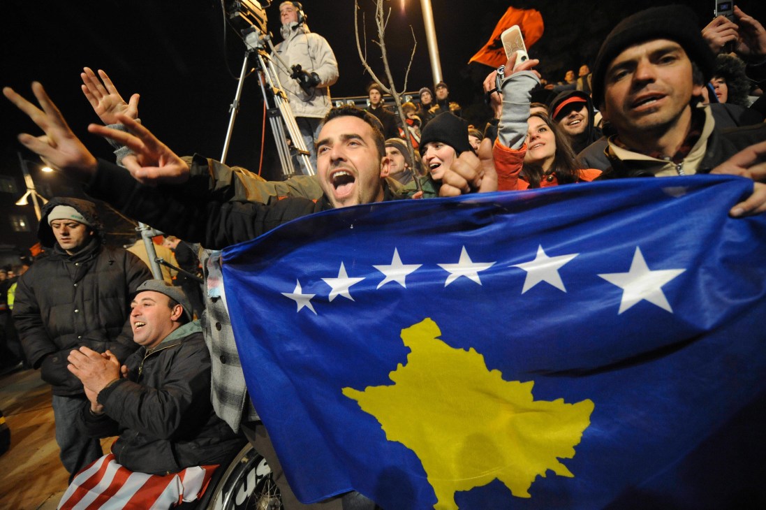 Kosovars celebrate with their new flag featuring a yellow map and six white stars on blue background at night in Pristina.