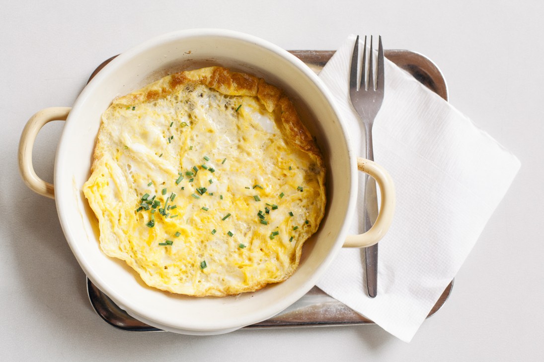 Omelet with chives in a cream-colored dish served with fork and napkin