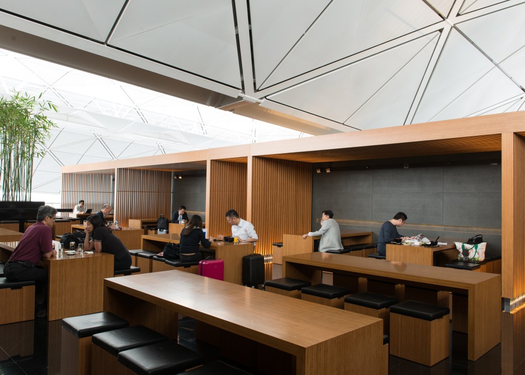 Modern airport lounge interior with wooden furnishings, geometric ceiling, and passengers dining.