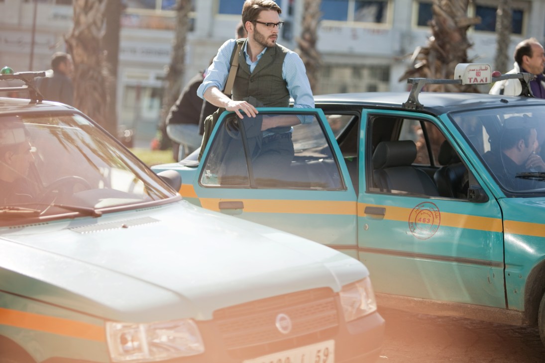 Man in layered menswear standing beside a turquoise and orange Tangier taxi cab.