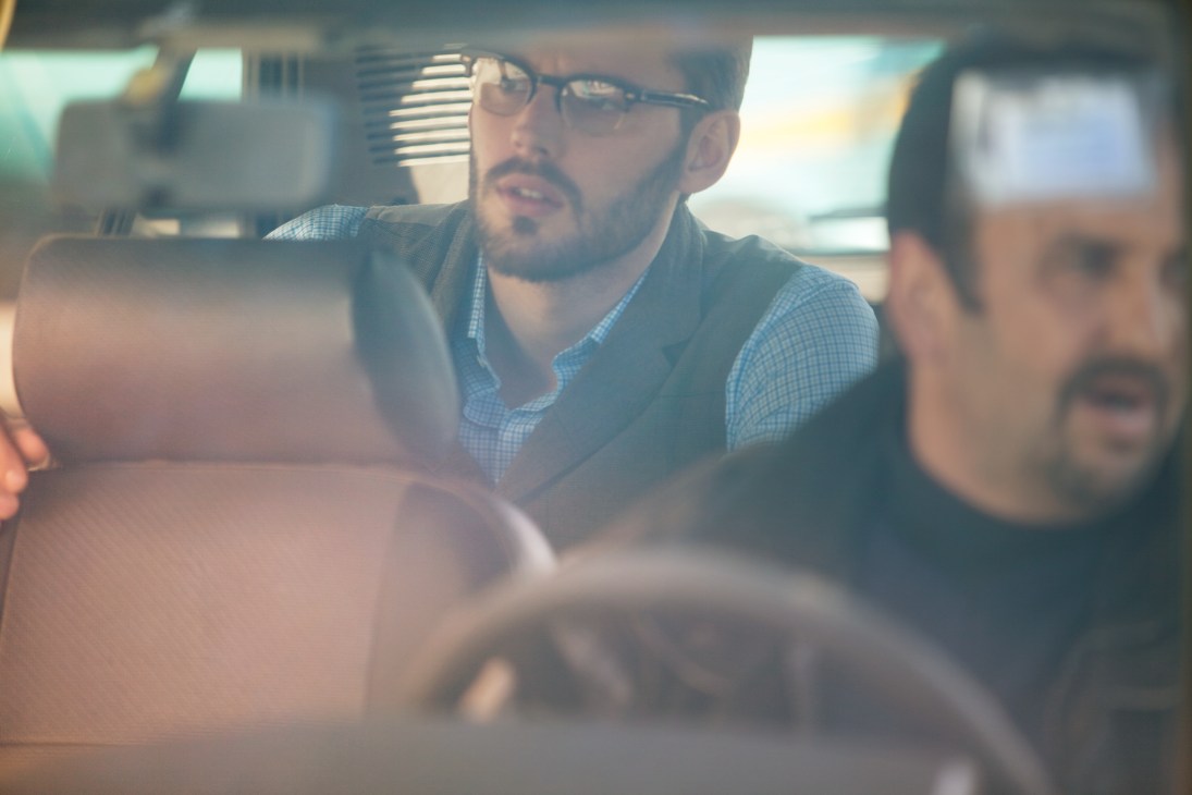 Man wearing glasses and blue checkered shirt in a car, styled with Ts(s) jacket, waistcoat and trousers.