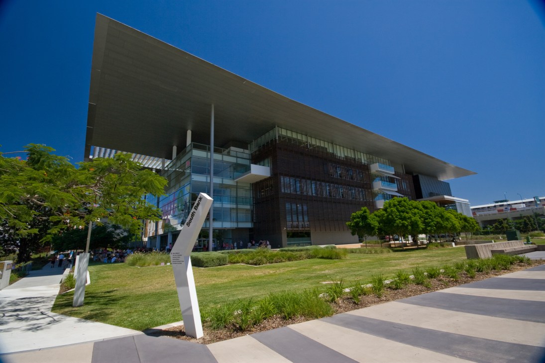 Modern architectural building with dark timber and glass facade beneath clear blue sky.