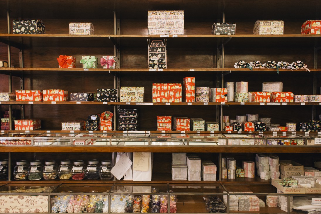Wooden shelves displaying colorful boxes of handmade chocolates at Altmann & Kühne confectionery shop in Vienna.
