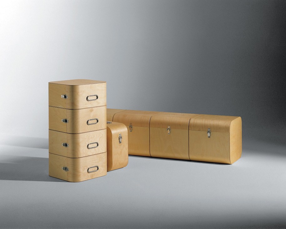 Wooden storage furniture by Schmidinger featuring stacked drawer units and a cylindrical trunk with metal handles.