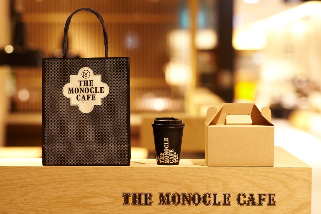 Monocle Café branded tote bag, coffee cup, and takeout box displayed on wooden counter