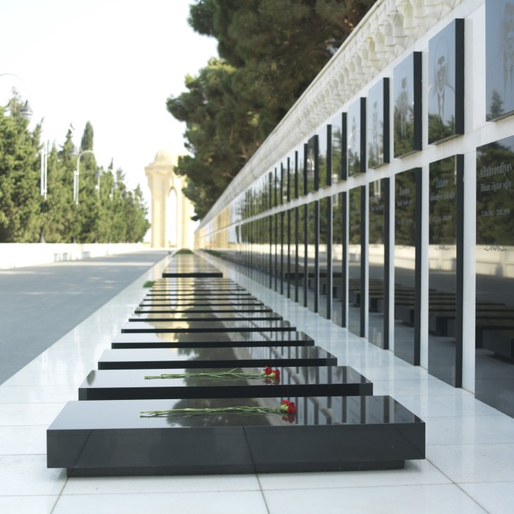 Memorial wall with black stone blocks holding red flowers honoring 1990 independence victims.