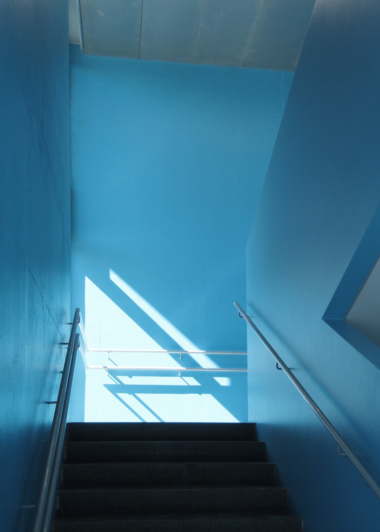 Bright blue stairwell with natural light streaming through skylight windows and metal handrails.