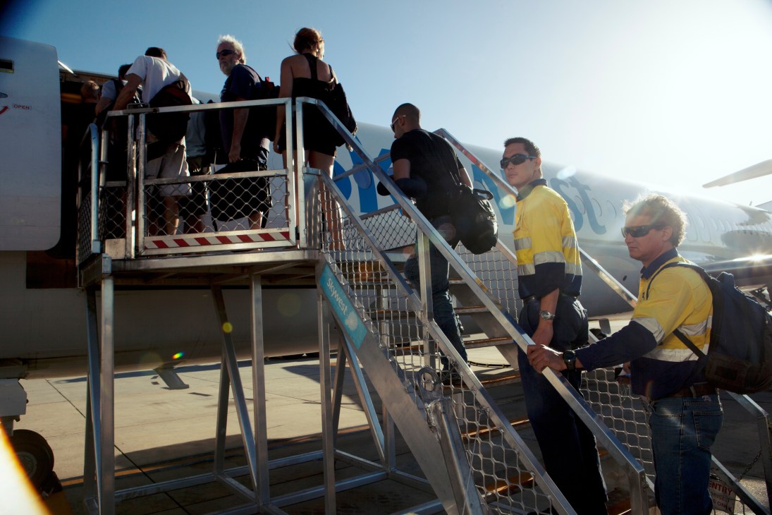 Fly-in-fly-out workers boarding a plane via stairs at Perth Airport, some wearing high-visibility vests.