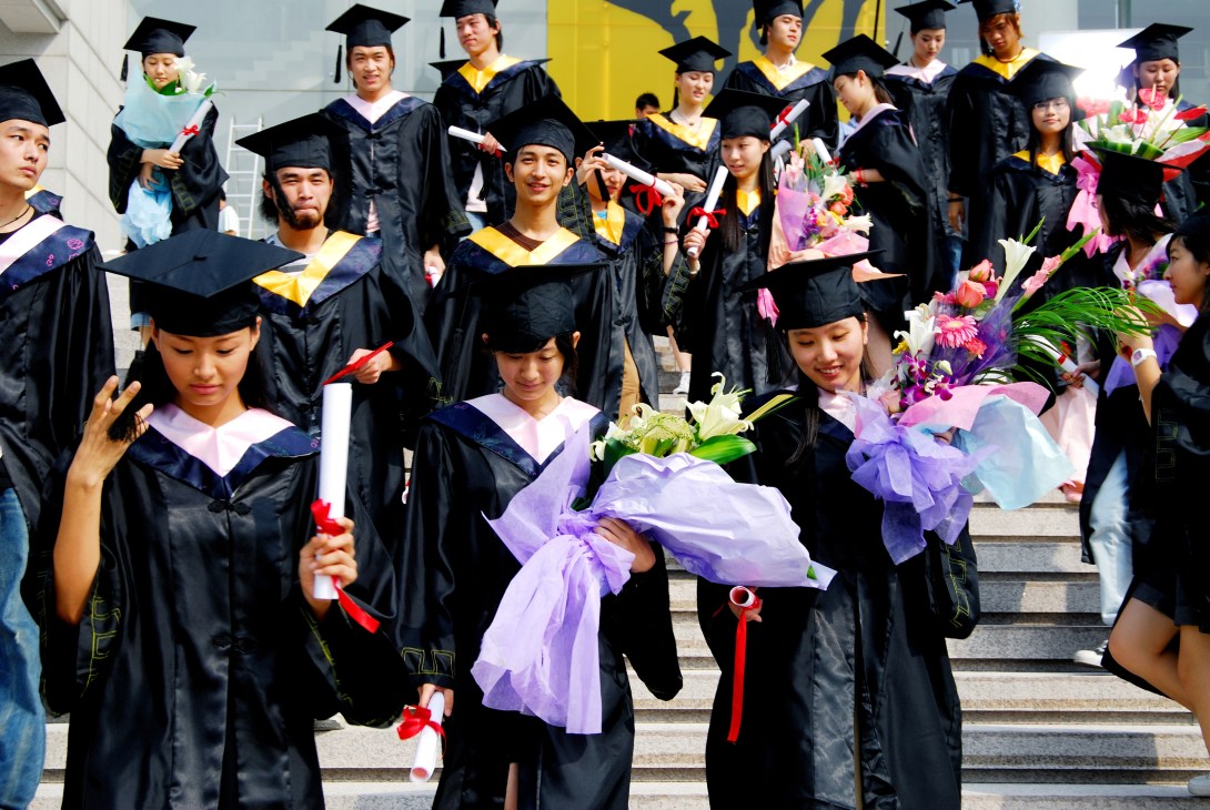 Taiwanese university graduates in black robes and mortarboards celebrate with diplomas and flowers.