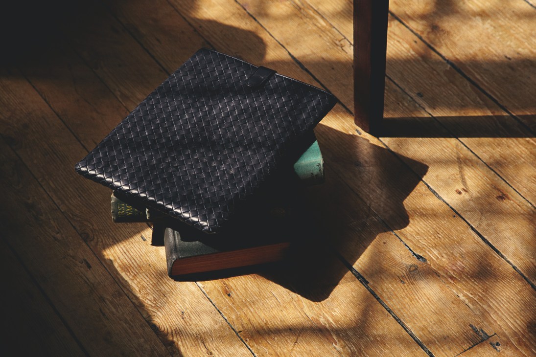 Bottega Veneta iPad case with woven leather detail on wooden floor in sunlight.