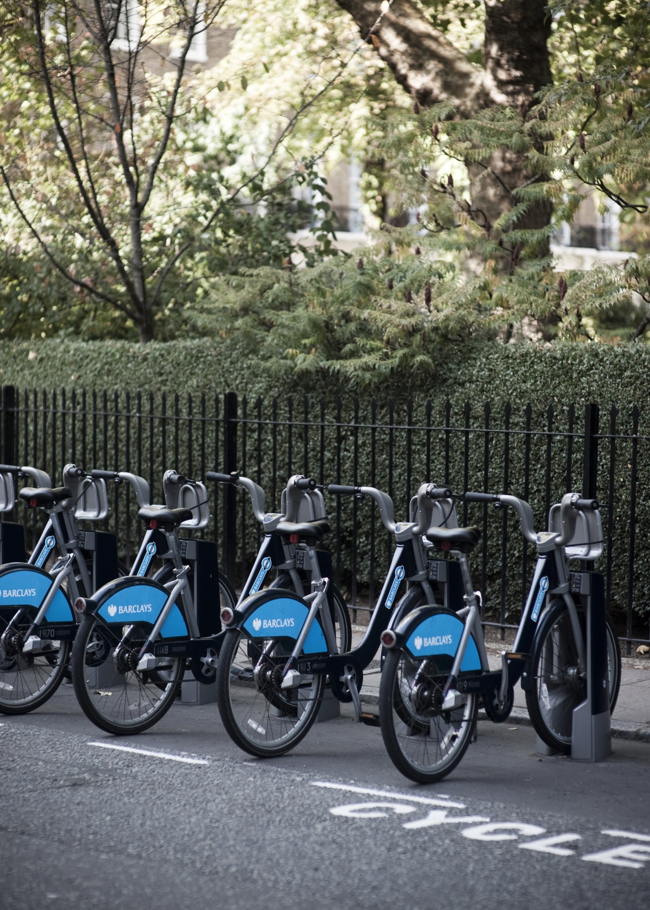 Row of blue and black Barclays-branded bicycles parked at a docking station on a London street.
